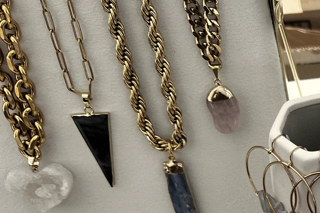 Gold chains from Drop 001 hanging on the display board with onyx, kyanite, rose quartz and clear quartz pendants